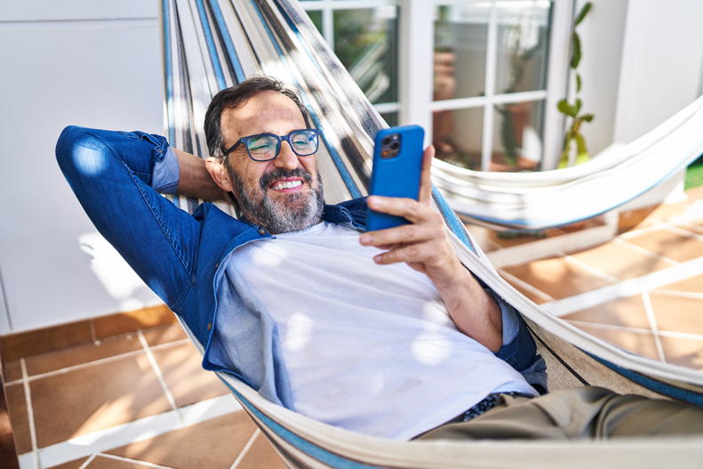Mann in einer Hängematte mit Handy in der Hand.